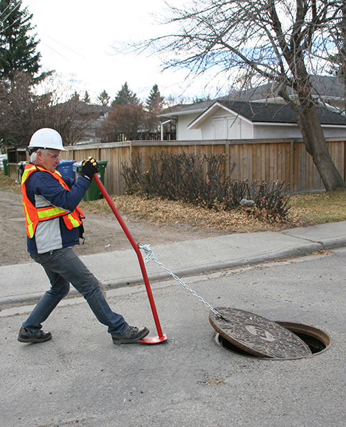 Utility worker removing manhole cover using Camlift lifter.